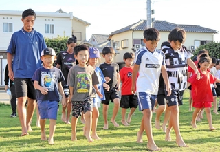 はだしで歩く感触を楽しむ子どもたちと指導した森岡亮太さん（左）＝稲美町国岡２