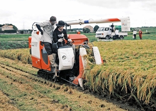 大竹宏樹さん（手前左）にコンバインの操作を教えてもらう学生＝稲美町草谷（ため池みらい研究所提供）
