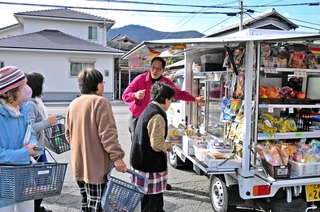 移動販売車「おまかせくん」が到着し、待ち構えた住民が買い物を始めた＝加古川市志方町西牧