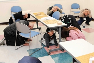 ラジオ放送を合図に、机の下に潜ったり、身をかがめたりしたシェイクアウト訓練の参加者ら＝稲美町加古