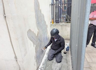 　１０日、ロンドンの裁判所の壁に描かれたバンクシーの新作を消す作業員（ＡＰ＝共同）