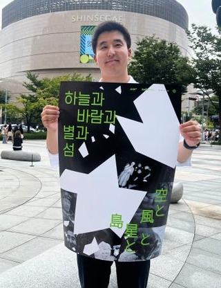 　映画「空と風と星と島」のポスターを手にする金明允さん＝１９日、韓国・釜山（共同）