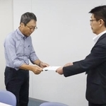 　米軍と日本政府に抗議を求める文書を手渡す地元市民団体の久米慶典共同代表（左）＝１８日午前、山口県岩国市役所