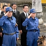 　慰霊碑の前で敬礼する警察犬の担当者＝２３日午前、東京都板橋区