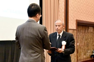 　「地域貢献大賞」の表彰式で日本新聞協会の中村史郎会長（左）から大賞の記念の盾を受け取る北國新聞宝立販売所の船本寛所長＝２０日午後、東京都千代田区