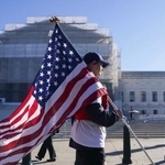 　米連邦最高裁の外を米国国旗を持って歩く人＝５日、ワシントン（ロイター＝共同）