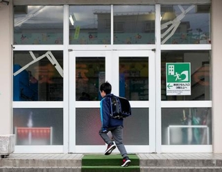 　学校が再開し、登校する青森県八戸市立江南小の児童。地震でガラス扉がひび割れた＝１０日午前７時４７分
