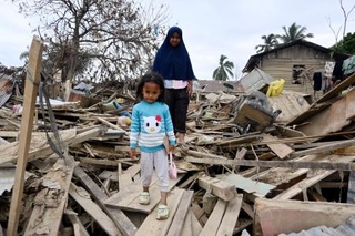 　がれきを通り、家から外出する親子＝２６日、インドネシア・クアラシンパン（共同）