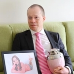 　オーストラリア・メルボルン郊外の自宅で、娘のオリビアさんの遺影と骨つぼを手にするロブ・エバンズさん＝１１月（共同）