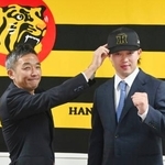 　現役ドラフトでヤクルトから阪神に移籍し、帽子をかぶせてもらう浜田（右）＝１２日、兵庫県西宮市