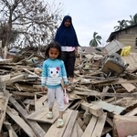 　がれきを通り、家から外出する親子＝２６日、インドネシア・クアラシンパン（共同）