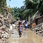 　がれきが積み上がる住宅街を歩く少年＝２５日、インドネシア・クアラシンパン（共同）