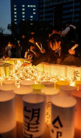 　「１・１７のつどい」が開かれる会場で、紙灯籠に火をともす人たち＝１６日夕、神戸市中央区