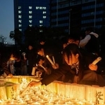 　「１・１７のつどい」が開かれる会場で、紙灯籠に火をともす人たち＝１６日夕、神戸市中央区