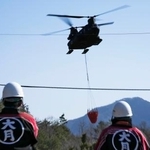 　消火活動を行う陸上自衛隊のヘリコプターを見つめる地元消防団の人たち＝１８日午後、山梨県大月市
