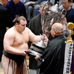 　大相撲初場所で２場所連続優勝を果たし、日本相撲協会の八角理事長（右）から賜杯を受け取る安青錦。新大関での優勝は史上９人目の快挙となった＝２５日、東京・両国国技館