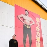 　「プロレス殿堂館」の壁に掲げた力道山の肖像の前に立つ永田章一館長＝２０２５年１２月、熊本県天草市