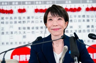 　当確者の名前のバラの前で、メディアのインタビューに笑顔で答える自民党総裁の高市首相＝８日午後１０時３分、東京・永田町の党本部