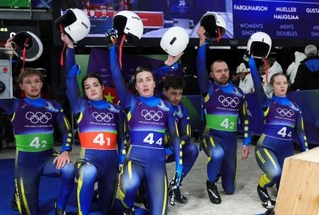 　リュージュのチームリレーで、ゴール後に片膝をついてヘルメットを掲げるウクライナ代表の選手たち＝コルティナダンペッツォ（ロイター＝共同）