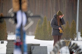 　ロシアのウクライナ侵攻開始から４年となった２４日、首都キーウ近郊イルピンにある夫デニスさんの墓の前で涙をぬぐうイアナ・サクンさん（共同）