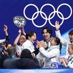 　団体男子ＳＰの得点を確認し、坂本花織（前列右から２人目）と手を合わせて喜ぶ鍵山優真＝ミラノ（共同）