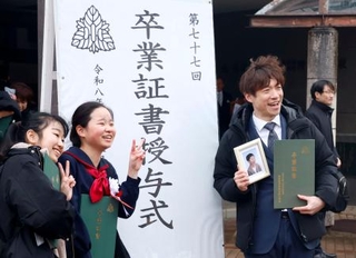 　長男泰介さんの写真と卒業証書を手に、泰介さんの友人らと記念写真に納まる大間圭介さん＝１３日午後、金沢市