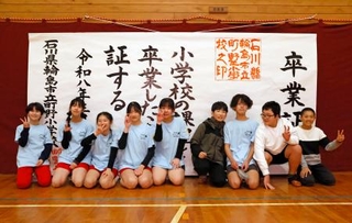 　大きな紙でできた「卒業証書」の前で、記念写真に納まる川原脩伸さん（右端）ら＝２１日午後、石川県輪島市の町野小