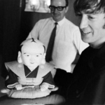 　福助人形を手にほほ笑む英ロックバンド「ビートルズ」のジョン・レノンさん。１９６６年の来日公演で撮影された写真１０２枚分のネガフィルムが見つかった（日本武道館提供）