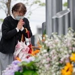 　熊本地震の「前震」から１０年となり、震災記念公園で献花し手を合わせる女性＝１４日午前、熊本県益城町