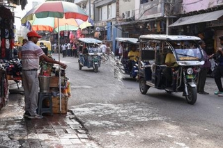 　２７日、インド・ニューデリーで路上に水をまく男性（共同）