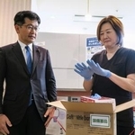 　配送された国備蓄の医療用手袋を着ける「天王洲パークサイドビル歯科」の坂田香里院長。左は厚労省の仁木博文副大臣＝２３日午後、東京都品川区