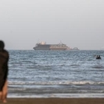 　ホルムズ海峡通過の許可を待つ貨物船と、ペルシャ湾沿岸に見える人々＝１５日、イラン・バンダルアバス（ゲッティ＝共同）