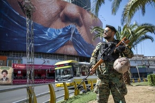 　イランの首都テヘランで、ホルムズ海峡の形をした青いリボンで口をふさがれたトランプ米大統領のポスターの前に立つ警察官＝５月（ゲッティ＝共同）