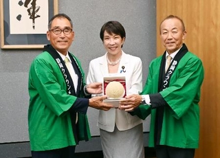 　静岡県温室農業協同組合クラウンメロン支所の沢木勝支所長（左）らから「クラウンメロン」を受け取る高市首相（中央）＝８日午後、首相官邸（山本裕三事務所提供）