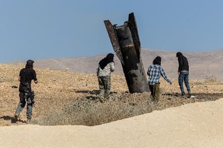 　８日、ヨルダン川西岸で、着弾したイランのミサイルのそばに立つイスラエル人入植者（ロイター＝共同）