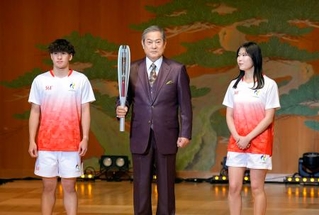 　愛知・名古屋アジア大会の開幕まで１００日となり、セレモニーで聖火リレーのユニホーム（左右）とともにトーチを披露する松平健さん＝１１日午前、名古屋市