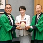 　静岡県温室農業協同組合クラウンメロン支所の沢木勝支所長（左）らから「クラウンメロン」を受け取る高市首相（中央）＝８日午後、首相官邸（山本裕三事務所提供）