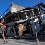 　フィリピンのミンダナオ島で、地震により倒壊した建物のそばを通り過ぎる女性＝９日、ジェネラルサントス（ロイター＝共同）