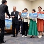　政府側（手前）に署名を渡す議連メンバーら＝１８日午後、国会内