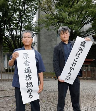 　上告審判決を受け、最高裁前で「原告適格認める」と書かれた紙を掲げる原告の金城武政さん（左）＝１３日午後