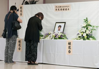 　高知競輪場に設置された伏見俊昭さんの献花台で手を合わせる人たち＝２０日、高知市
