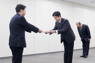 　総務省の担当者から行政指導の文書を受け取るＫＤＤＩの松田浩路社長（中央）＝２９日午後、東京都千代田区