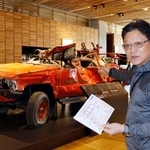 　東日本大震災津波伝承館の被災消防車の前で、謎解きについて説明する「キャピタルホテル１０００」の松田修一社長＝４月、岩手県陸前高田市