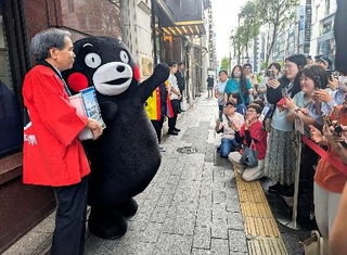 　「銀座熊本館」の前で客に手を振る「くまモン」。左端は前熊本県知事の蒲島郁夫さん＝２２日午前、東京・銀座