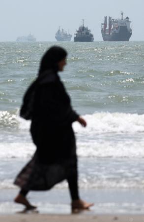 　ホルムズ海峡に臨む海岸を歩く女性。沖合には船舶が浮かんでいる＝２５日、イラン南部バンダルアバス（ＷＡＮＡ提供、ロイター＝共同）