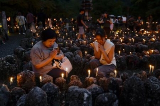 　化野念仏寺で始まった「千灯供養」で石仏に手を合わせる参拝者＝２９日夕、京都市右京区