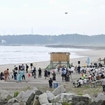 　東日本大震災後初めてとなる１６年ぶりの海開きが行われた請戸海水浴場。奥には東京電力福島第１原発の排気筒が見える＝１日午前、福島県浪江町
