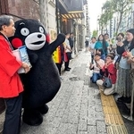 　「銀座熊本館」の前で客に手を振る「くまモン」。左端は前熊本県知事の蒲島郁夫さん＝２２日午前、東京・銀座