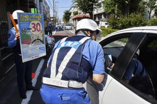 　ドライバーに生活道路の法定速度引き下げを周知する警視庁の警察官＝８月２５日、東京都世田谷区