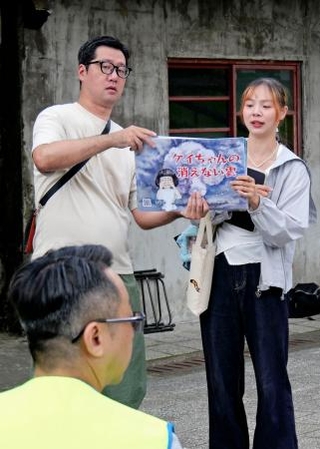 　紙芝居を手に取って参加者らに説明する吉村大作さん（左）＝２０日、台北市（共同）